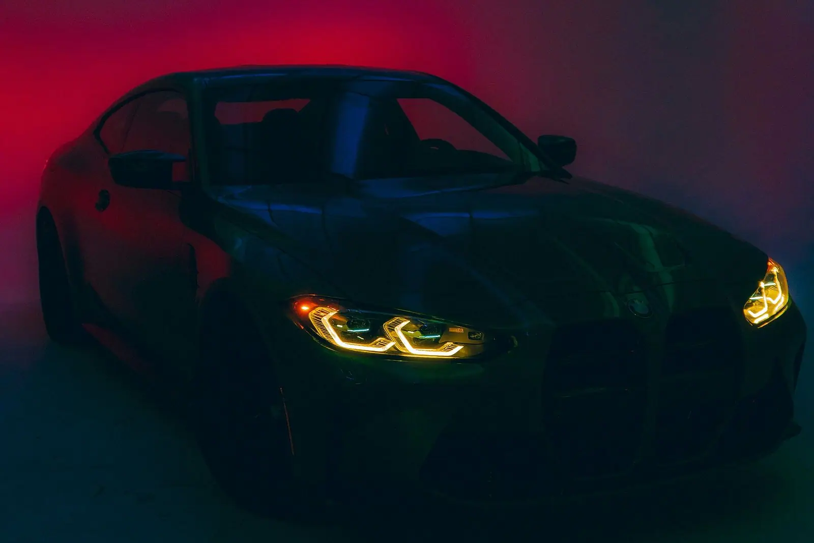 BMW M4 в студии с синим светодиодным потолком и красным светом, горят янтарные фары