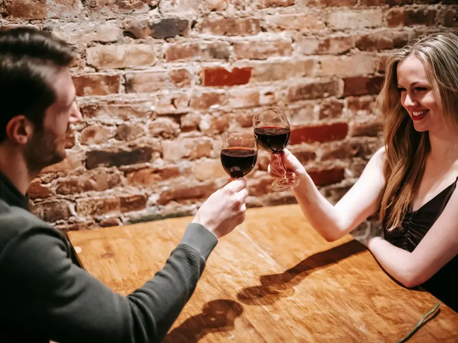 Пара чокается бокалами красного вина за деревянным столом