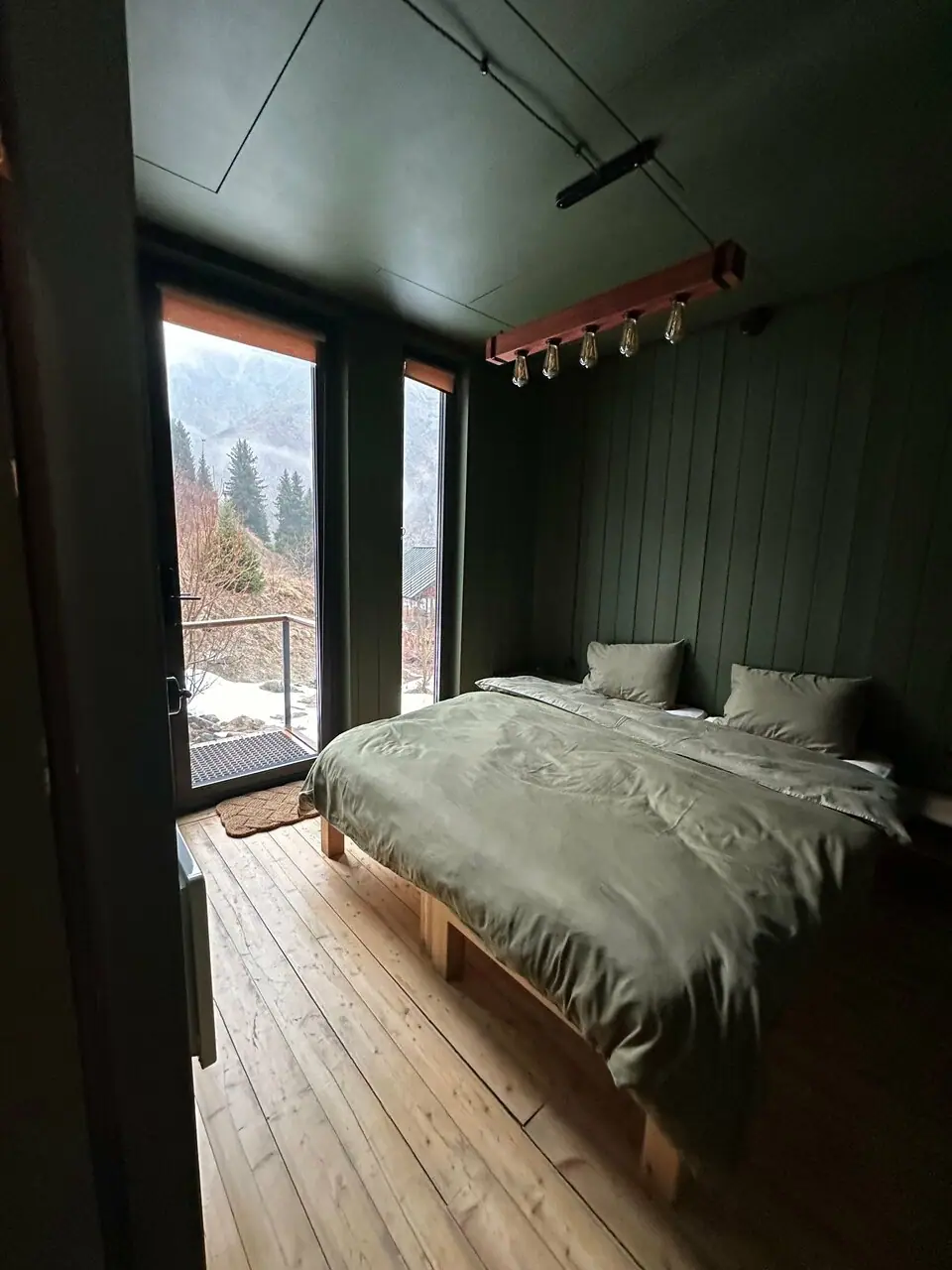 Спальня lodge зимой: кровать у стеклянной двери, за ней снег и ели