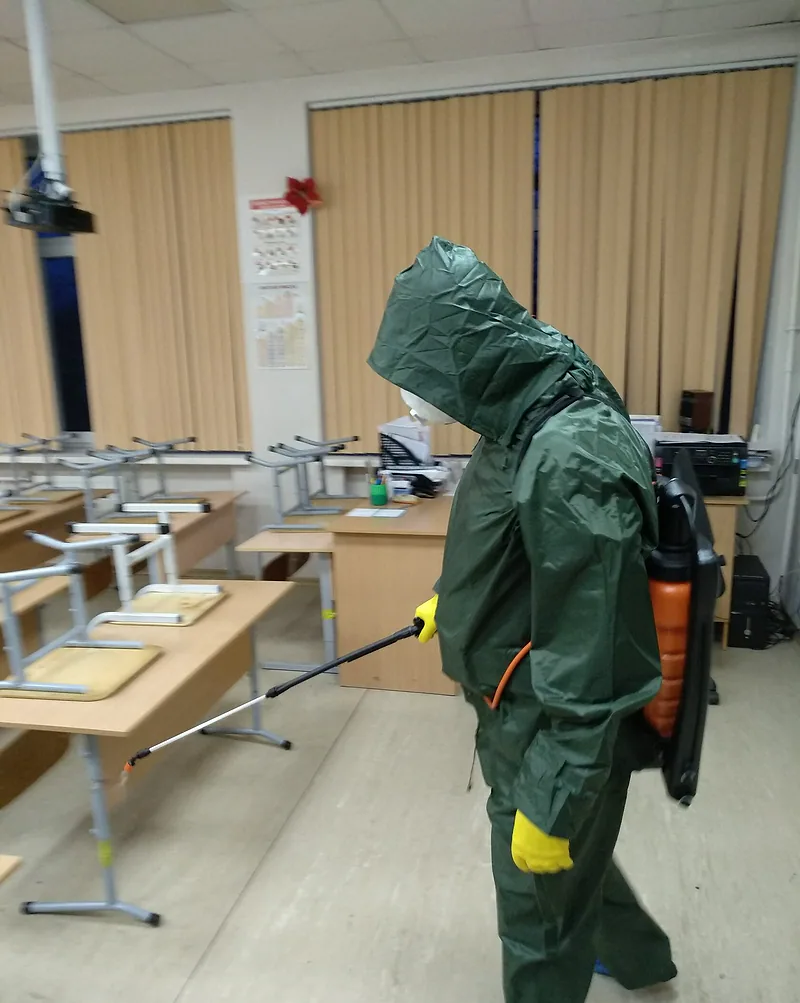 Дезинфекция класса: сотрудник в защитном костюме с ранцевым распылителем