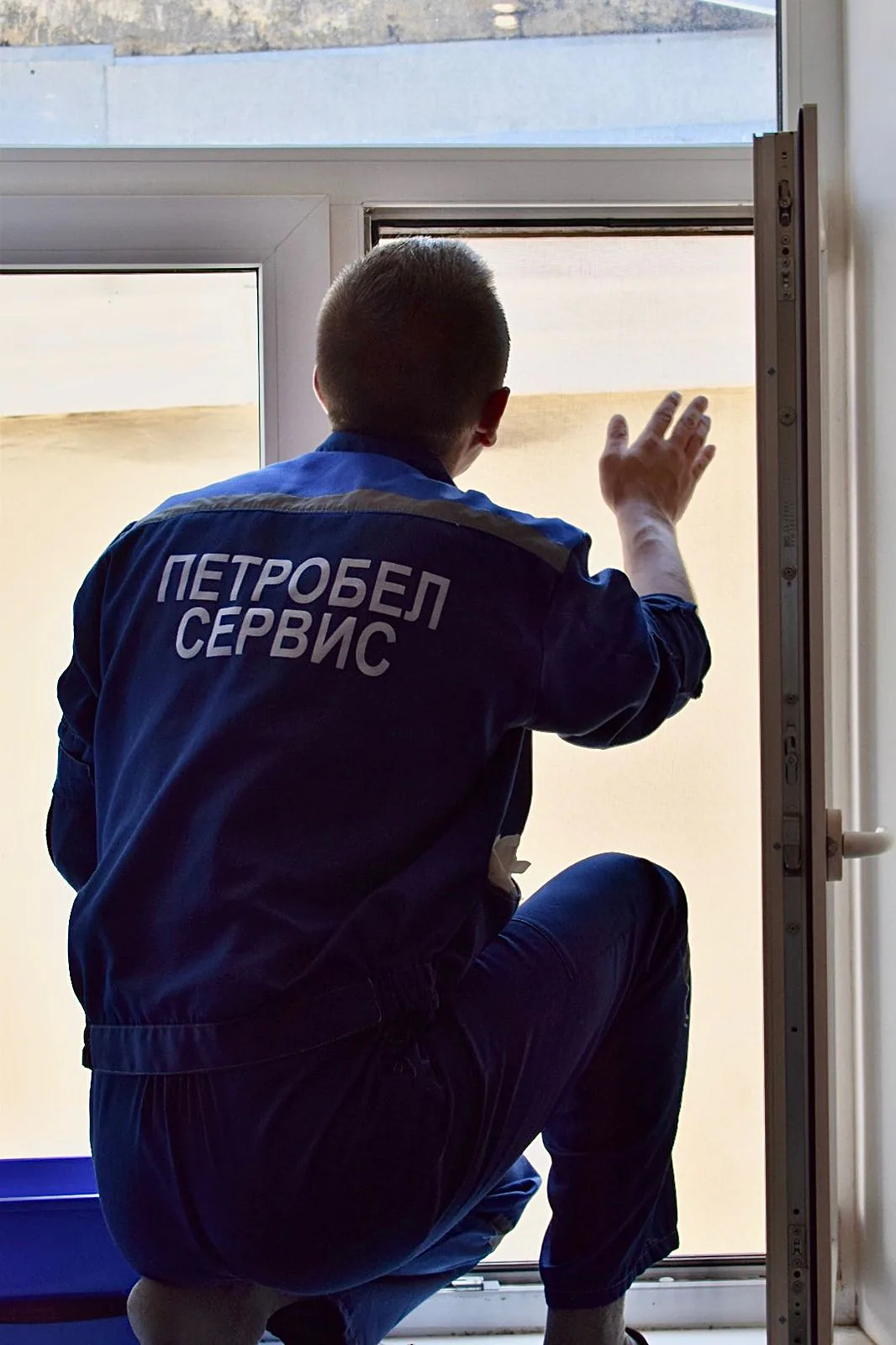 Сотрудник в куртке «ПетроБел сервис» моет окно