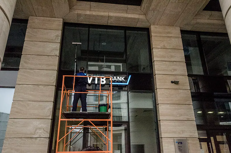 Тура у входа ВТБ, рабочий моет остекление над дверью
